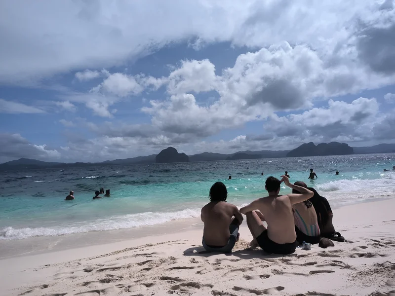 Small group of guests sitting together on a white-sand beach during island hopping in Palawan