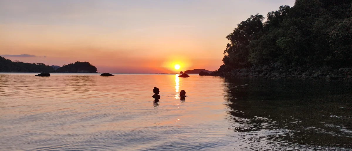 Two travelers swimming at sunset in the calm bay in front of DK2 Resort, Palawan